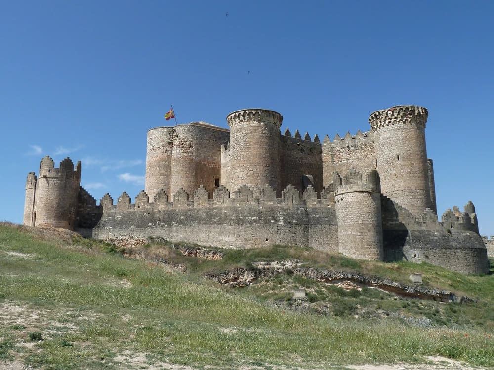 Belmonte Castle's six towers and Late Gothic battlements rising dramatically from the flat golden Manchegan meseta on a clear spring afternoon