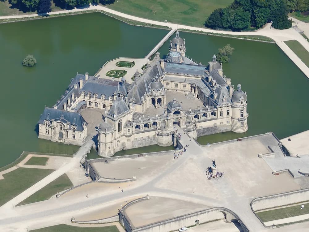 Château de Chantilly's Neo-Renaissance facade reflected in its moat, with André Le Nôtre's formal gardens stretching toward the canal