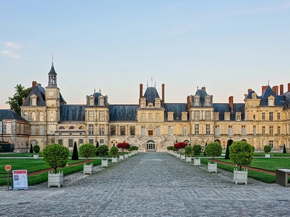 Château de Fontainebleau's classical facade reflected in the ornamental carp pond, with the formal parterre stretching towards the Fontainebleau forest