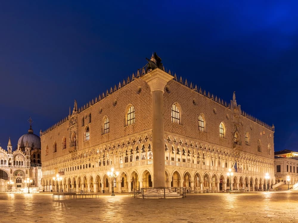The pink-and-white Gothic facade of the Doge's Palace rising above the columns of the Piazzetta San Marco at golden hour
