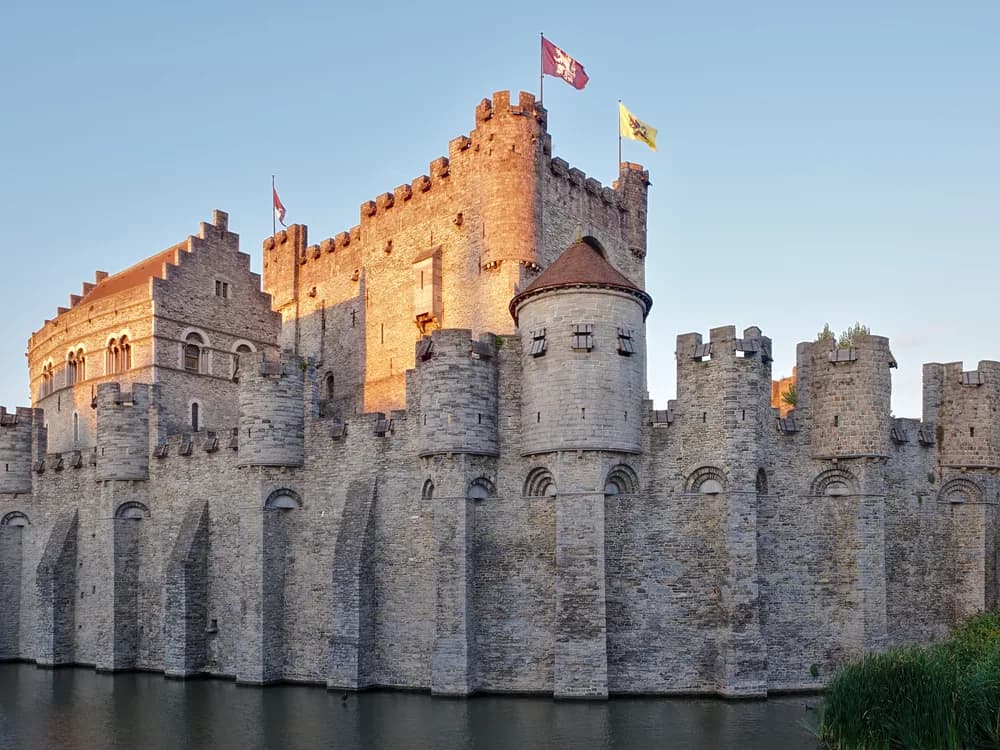 Gravensteen castle rising above the Ghent canals at dusk, with the medieval city roofline behind