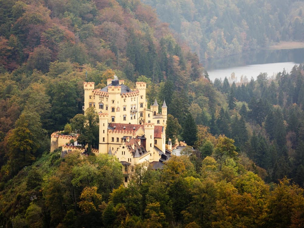 Hohenschwangau Castle rising above the forest with Alpsee lake below and the Bavarian Alps behind