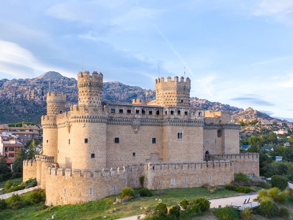 Manzanares el Real Castle's ornate Late Gothic towers reflected in the Santillana reservoir, with the dramatic granite peaks of La Pedriza rising behind