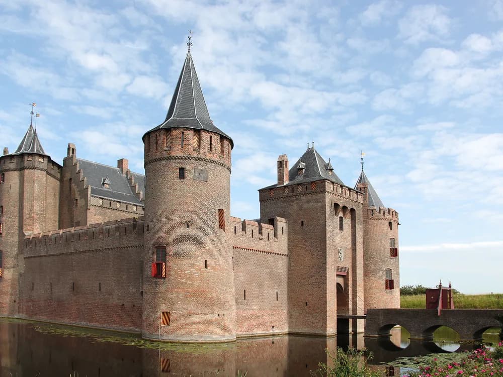 Muiderslot castle reflected in its moat on a still morning, its four towers perfectly symmetrical