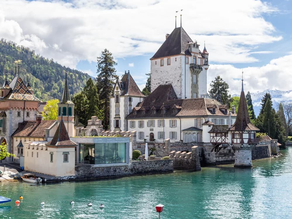 Oberhofen Castle (Schloss Oberhofen) rising from the southern shore of Lake Thun in the Bernese Oberland, Switzerland — the neo-Gothic towers of the 1849–52 Pourtalès renovation reflected in the Alpine lake