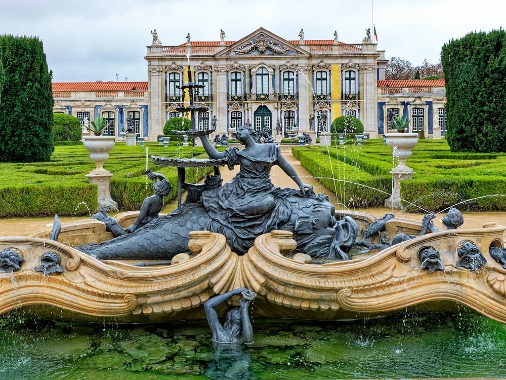 Queluz Palace's pink Rococo facade and formal gardens near Lisbon, with the Neptune Canal visible in the foreground
