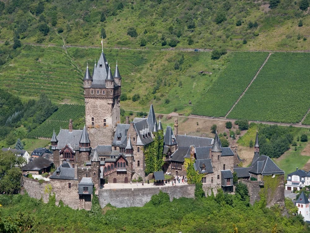 Reichsburg Cochem perched above the vine-covered hillsides of the Moselle River valley in Rhineland-Palatinate, its towers reflected in the river below