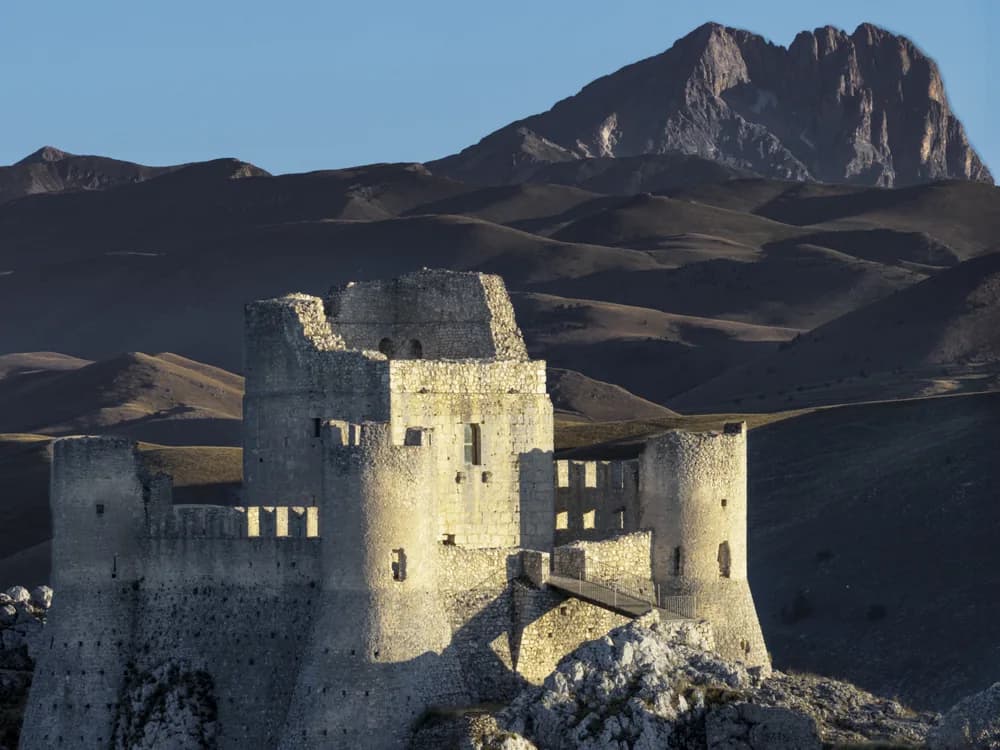 Rocca Calascio's square keep and circular corner towers standing alone on a high Apennine ridge in Abruzzo, with the Gran Sasso massif behind