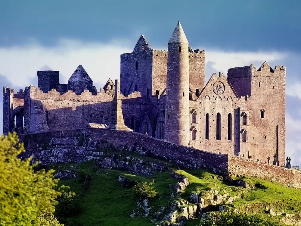 The Rock of Cashel rising above the Tipperary plain at dawn, its medieval towers silhouetted against a golden sky
