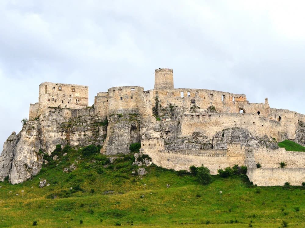 Spiš Castle's white limestone walls rising dramatically above the flat Spiš plain with the High Tatras visible in the distance