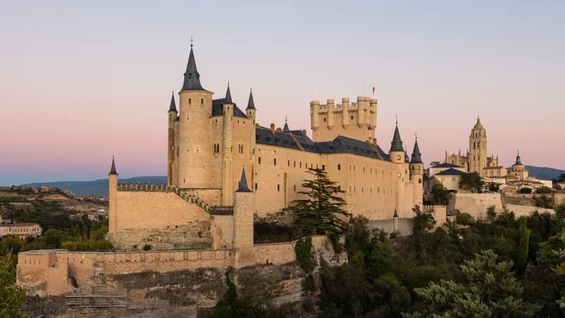 The Alhambra palace complex on its hillside above Granada, lit by late afternoon sun with the Sierra Nevada behind