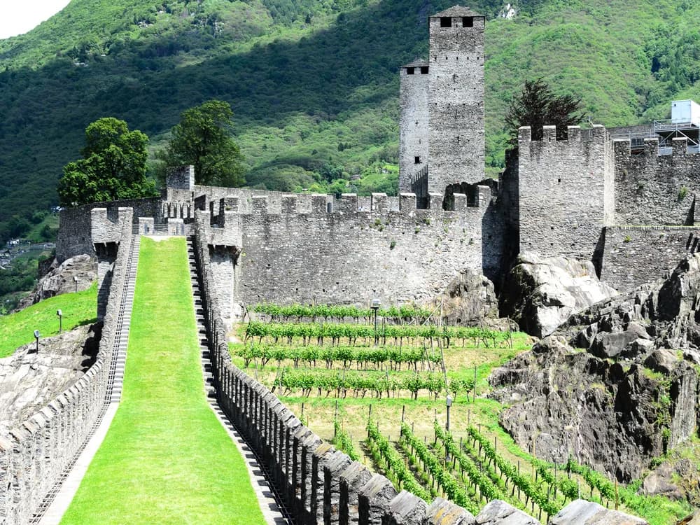 The three UNESCO World Heritage castles of Bellinzona, Switzerland — Castelgrande in the foreground with its twin towers, Montebello on the hill above, and Sasso Corbaro on the highest spur, connected by the Murata fortification walls