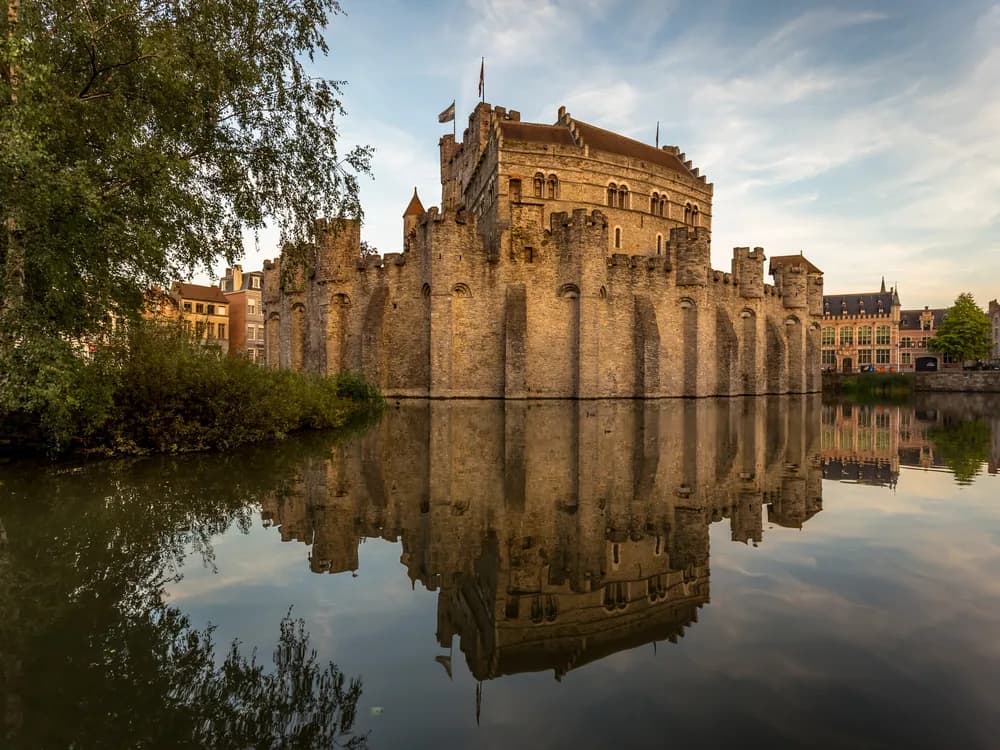 Gravensteen Castle rising from the Ghent canal network, its circular keep and towers reflected in the water