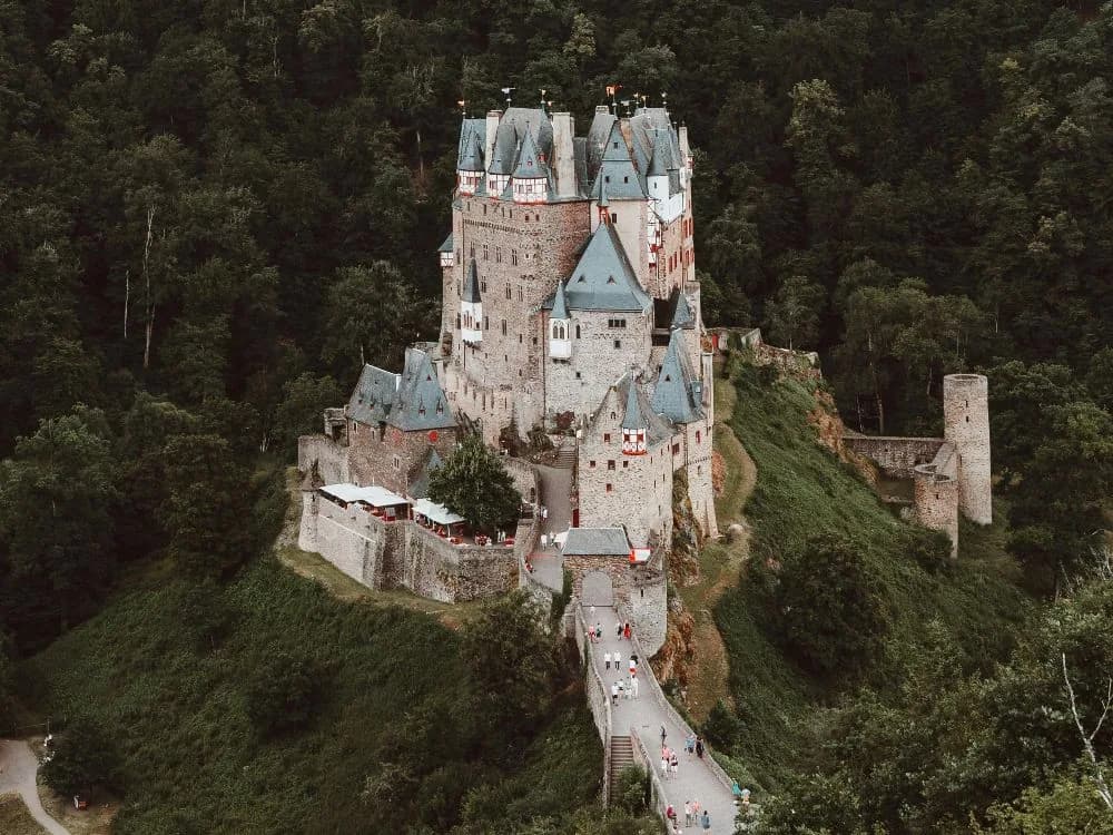 Eltz Castle emerging from the forested Moselle valley — its cluster of medieval towers rising above the trees