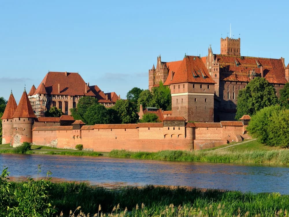 Malbork Castle's red brick towers reflected in the Nogat river at dusk