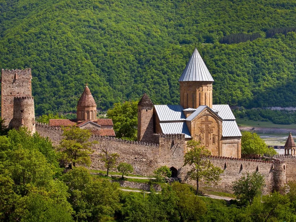 Ananuri Fortress towers reflected in the turquoise Zhinvali Reservoir with the Caucasus mountains behind