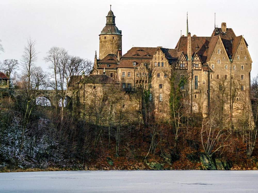 Czocha Castle on its promontory above Lake Leśniańskie — the 14th-century Silesian fortress with its 1909 Neo-Gothic reconstruction reflected in the artificial lake, near Leśna in Lower Silesia