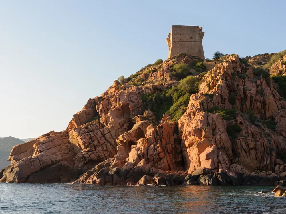Genoese Tower at Porto, Corsica — the 16th-century cylindrical watchtower on a red granite promontory above the Gulf of Porto, part of the UNESCO World Heritage coastal landscape