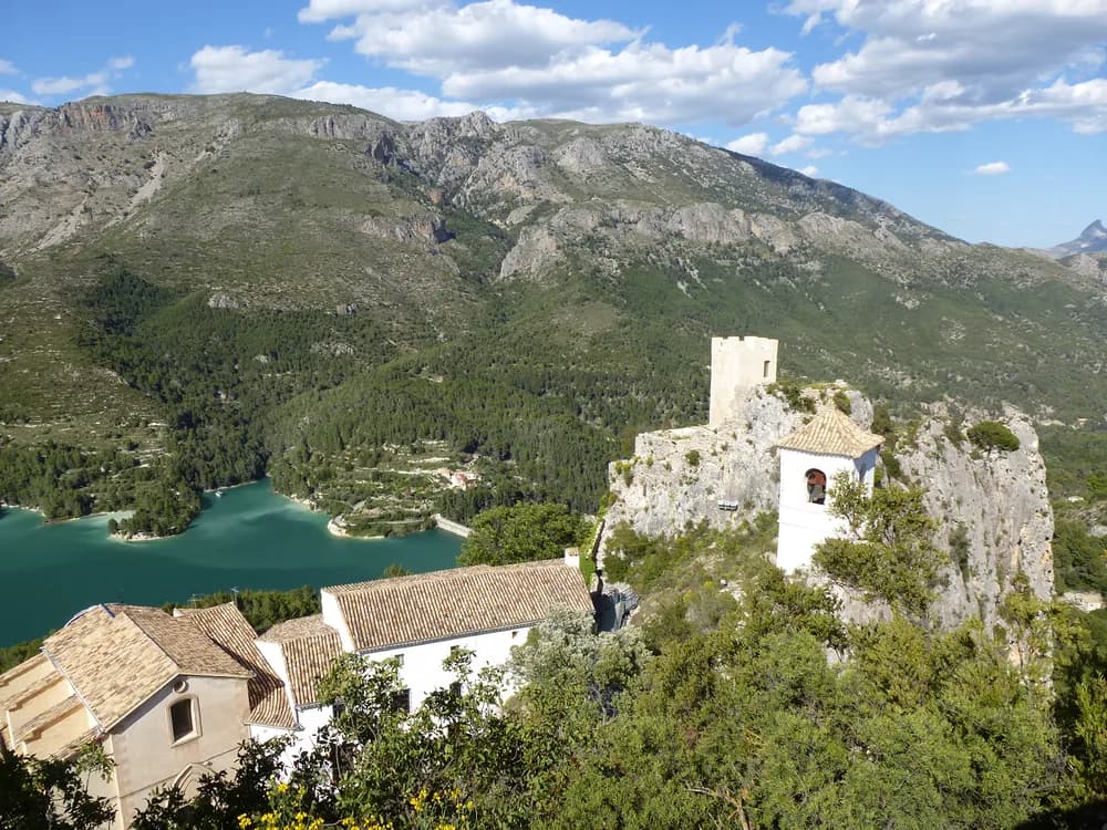 Guadalest Castle and fortified village on a limestone rock pinnacle above the turquoise Guadalest Reservoir in Alicante province, Spain — the medieval Moorish fortress taken by Jaime I of Aragon in 1258, damaged by the 1748 earthquake, and now one of Spain's most visited villages