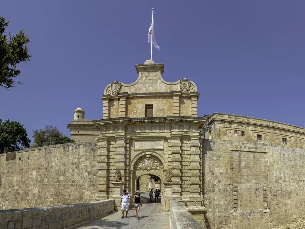 Mdina's Baroque gateway and limestone walls at dusk — the Silent City of Malta perched on its central ridge, with Rabat visible below
