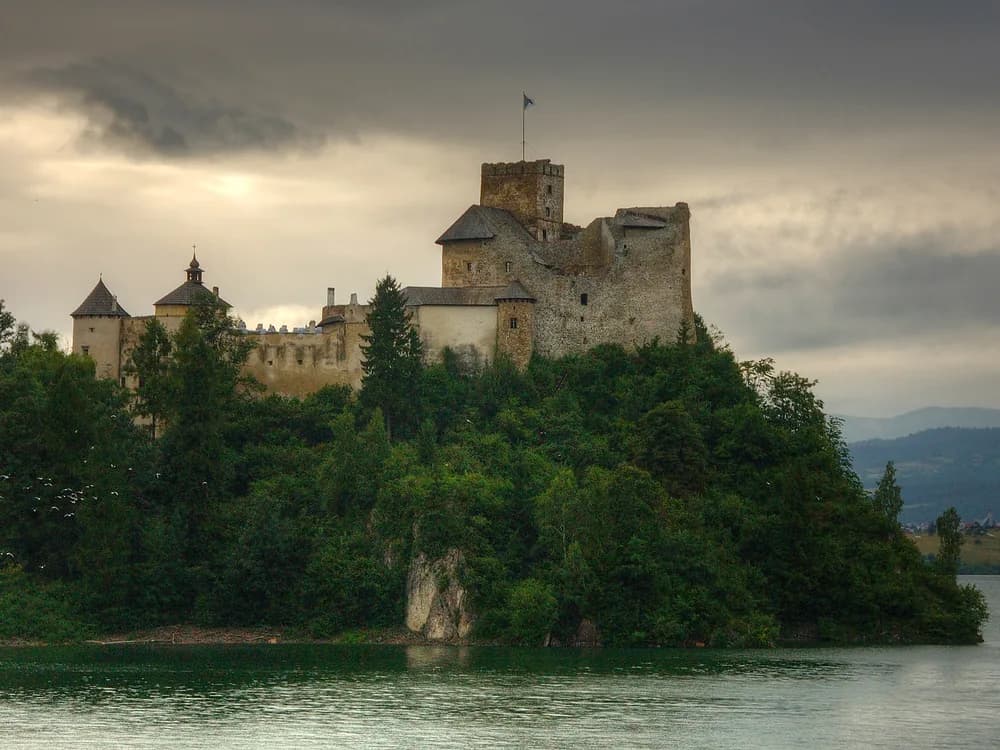 Niedzica Castle (Zamek Niedzica) above the turquoise Lake Czorsztyn in the Pieniny Mountains, Poland — the 14th-century Polish-Hungarian border castle on its promontory with the submerged ruins of Czorsztyn visible across the reservoir