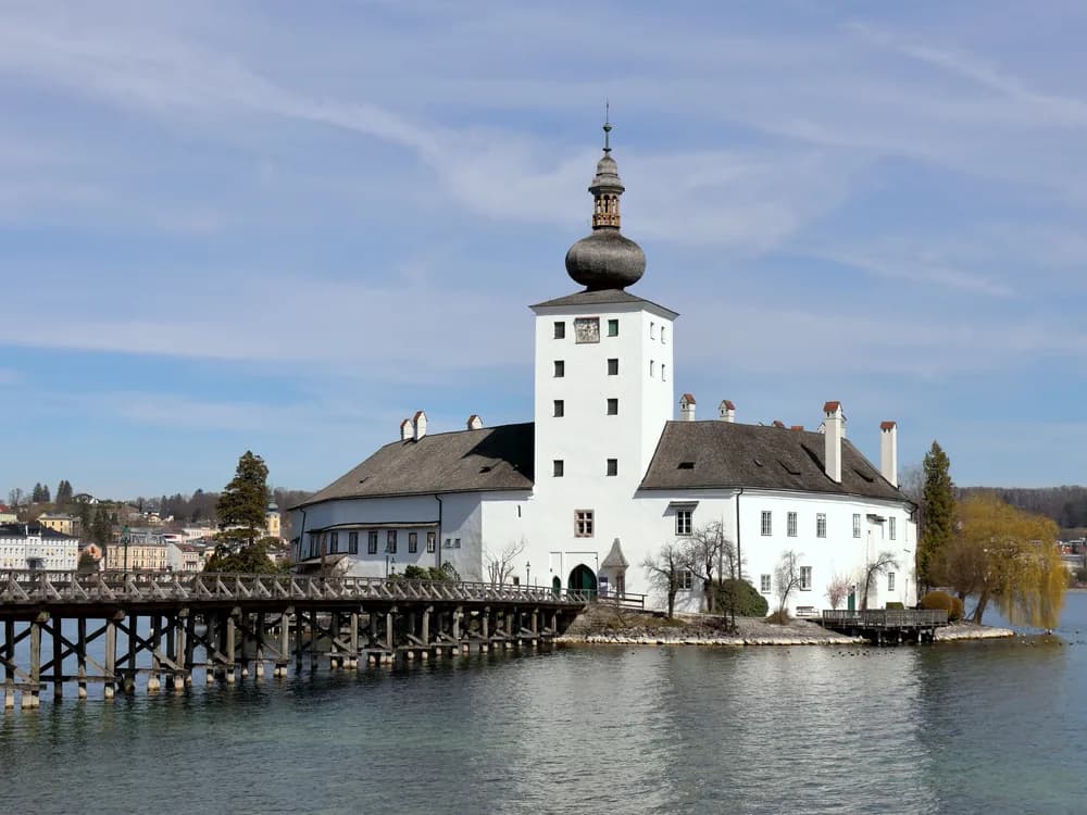 Schloss Ort on Lake Traunsee — the whitewashed medieval island castle in Gmunden, Upper Austria, seen from the wooden footbridge with the Traunstein peak beyond