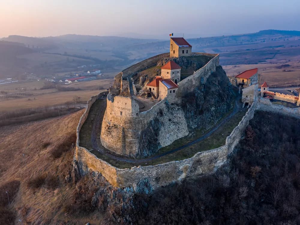 Viscri's UNESCO-listed fortified church in Transylvania — the whitewashed tower and defensive wall of the 12th-century Saxon church rising above the village rooftops, with the Transylvanian plateau behind