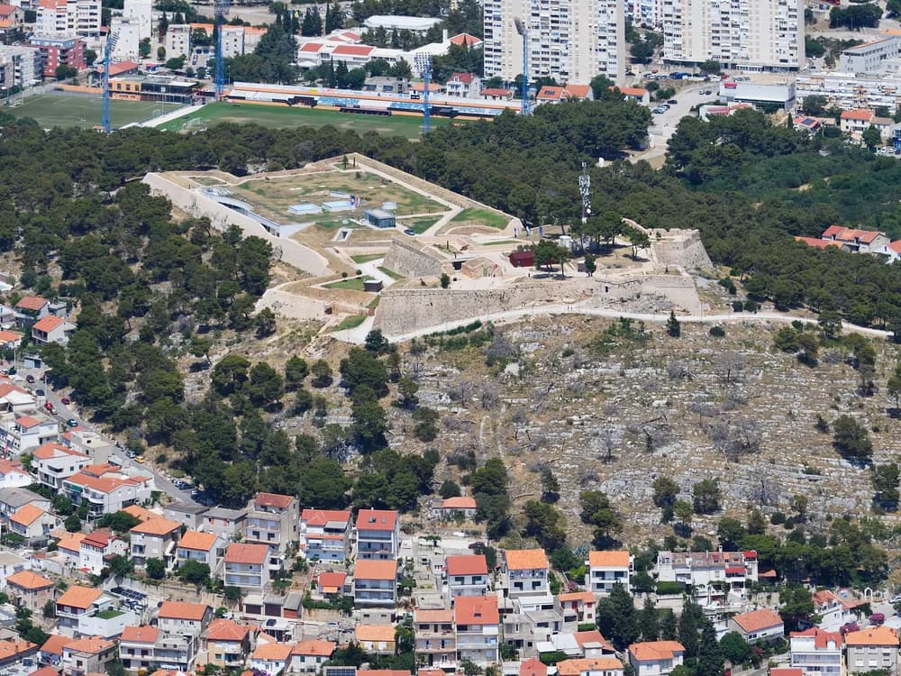 View from St. John's Fortress (Šubićevac) over Šibenik's old town, the cathedral dome, and the Adriatic channel below, with Barone Fortress visible on the neighbouring hill