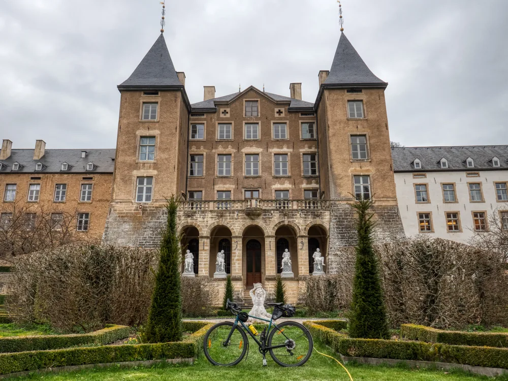 Ansembourg Castle in the Valley of the Seven Castles, Luxembourg — the 13th-century medieval Old Castle on its rocky spur above the Eisch river valley, with the 17th-century Baroque New Castle and terraced gardens below