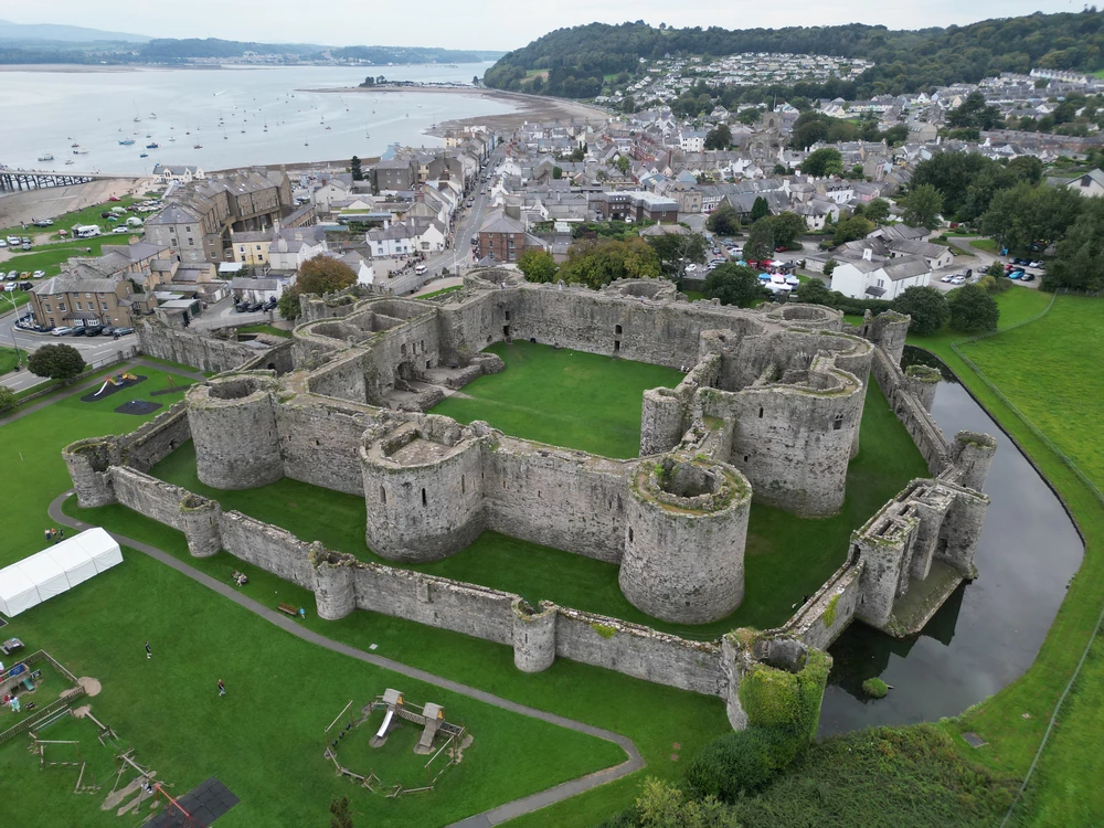 Beaumaris Castle's perfectly symmetrical concentric walls and towers reflected in the surrounding moat, Anglesey, Wales