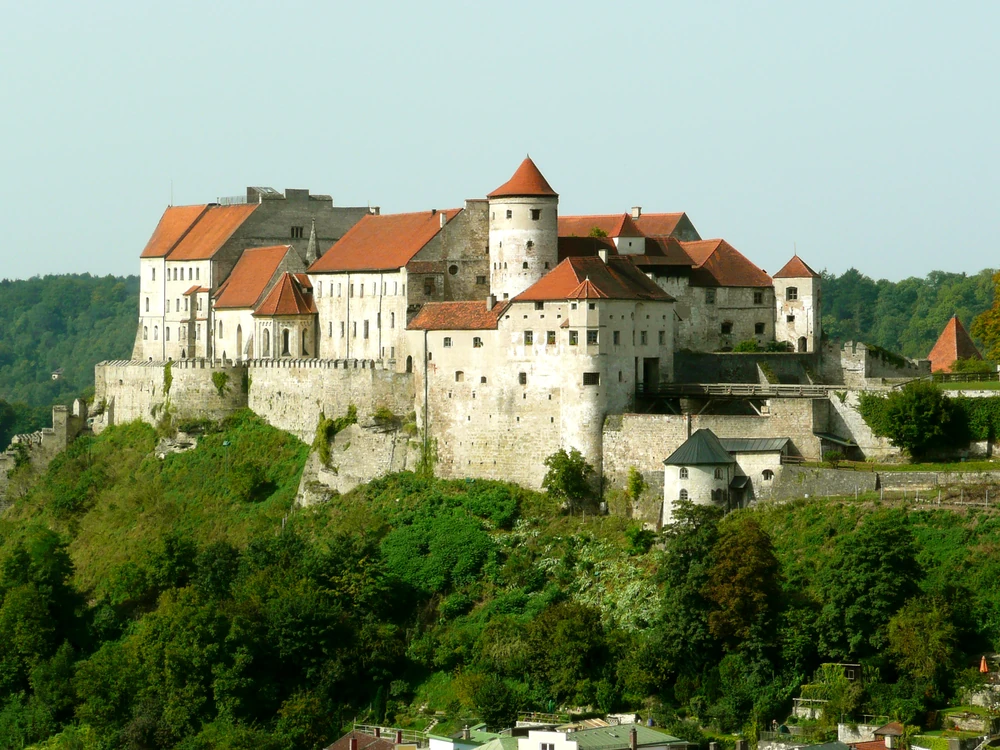 Burghausen Castle stretching along its limestone ridge above the turquoise Salzach River and Wöhrsee lake, with the Austrian Alps on the horizon