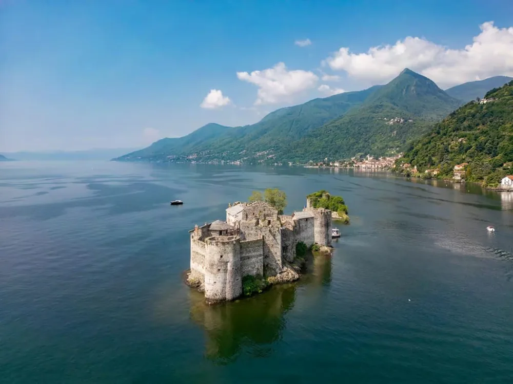 Castelli di Cannero on their rocky islets in Lake Maggiore, northern Italy — the twin ruined tower fortresses of the Mazzarditi pirate brothers (1403) and the Borromeo Rocca Vitaliana (1519), with the Swiss Alps visible to the north