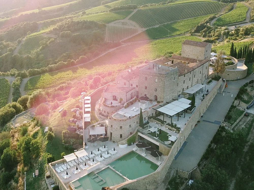 Castello di Velona near Montalcino, Tuscany — the medieval hilltop castle above the Brunello vineyards, now a luxury resort and thermal spa with infinity pool views over the Val d'Orcia UNESCO landscape