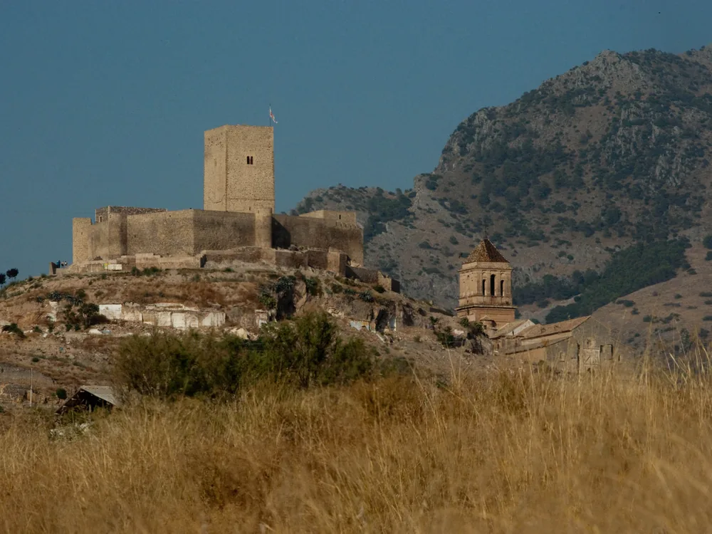 Castle of Alcaudete on its limestone hilltop above the olive groves of Jaén province — the frontier fortress of the Order of Calatrava, with the Torre del Homenaje and defensive walls spanning Caliphate, Almohad, and Christian military-order periods