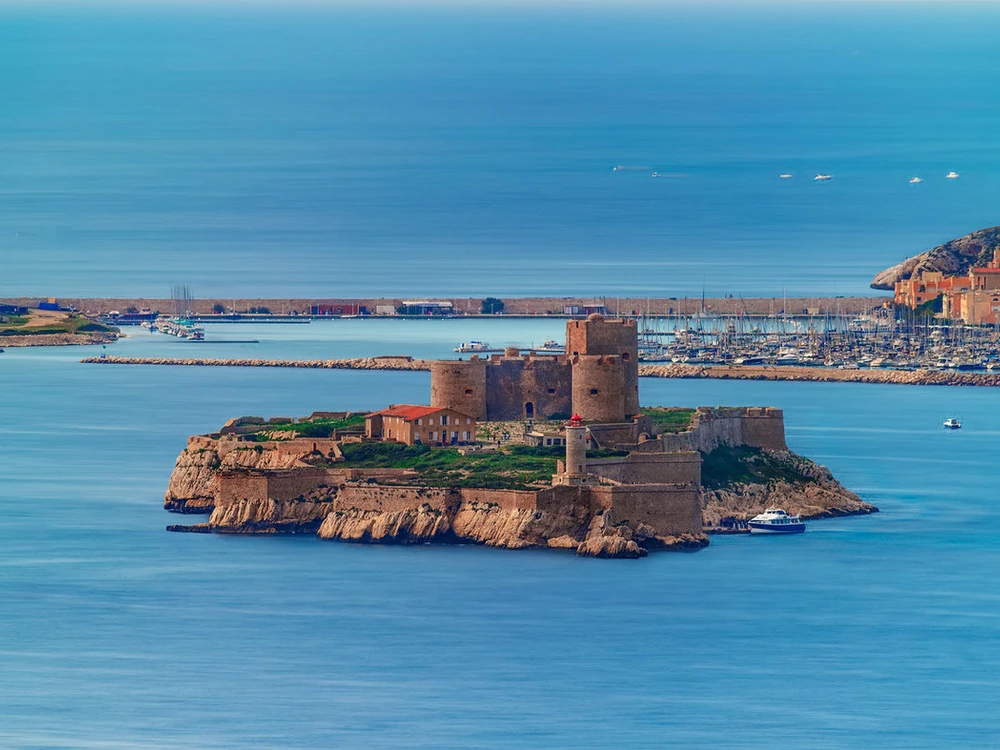 Château d'If rising from the Mediterranean Sea, its pale stone towers seen from a ferry approaching from Marseille's Vieux-Port