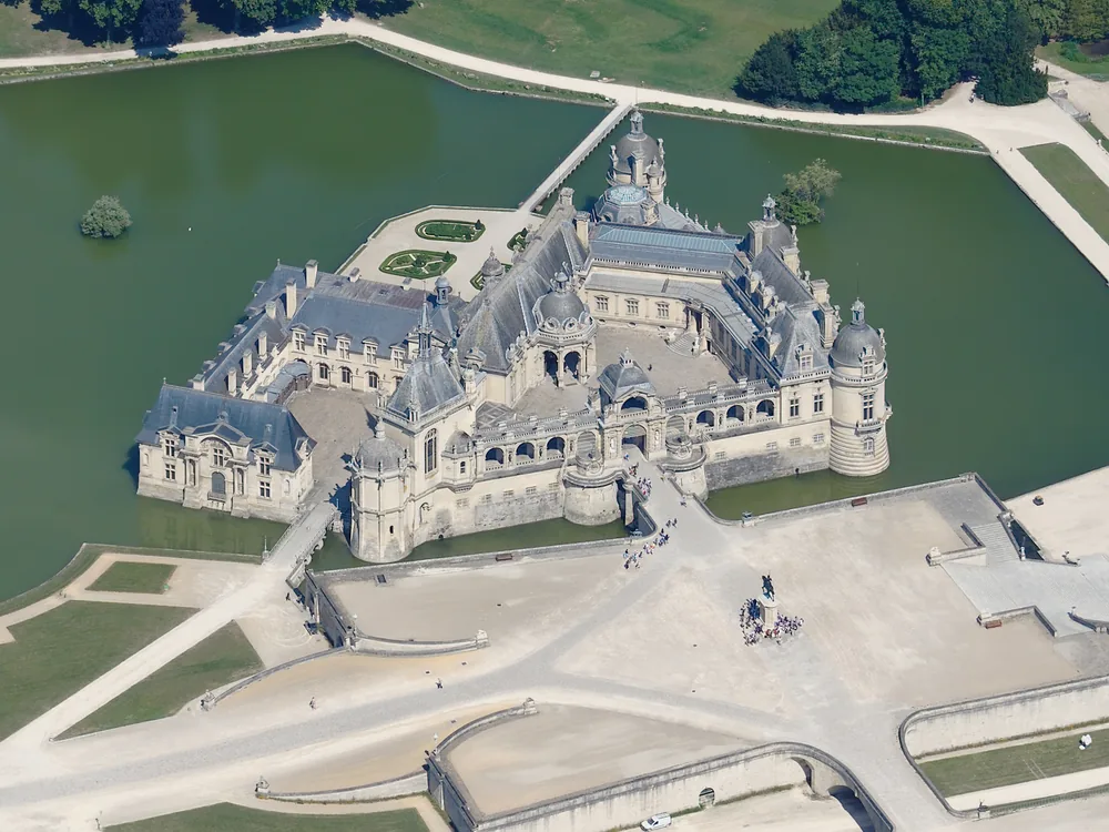 Château de Chantilly's Neo-Renaissance facade reflected in its moat, with André Le Nôtre's formal gardens stretching toward the canal