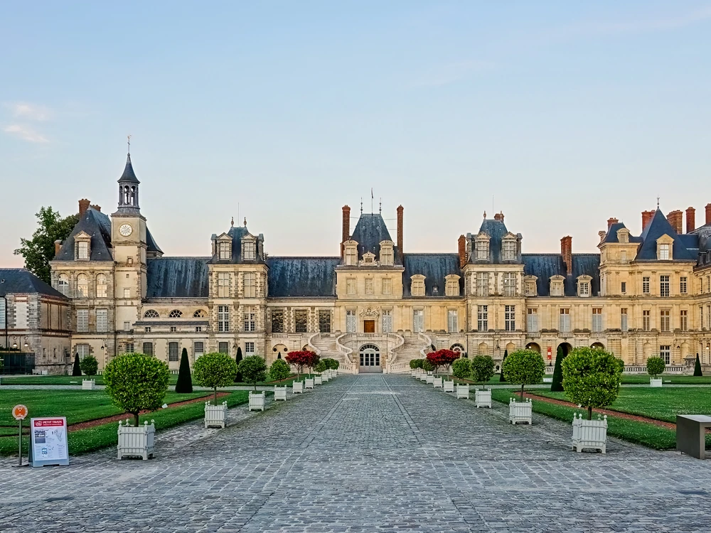 Château de Fontainebleau's classical facade reflected in the ornamental carp pond, with the formal parterre stretching towards the Fontainebleau forest