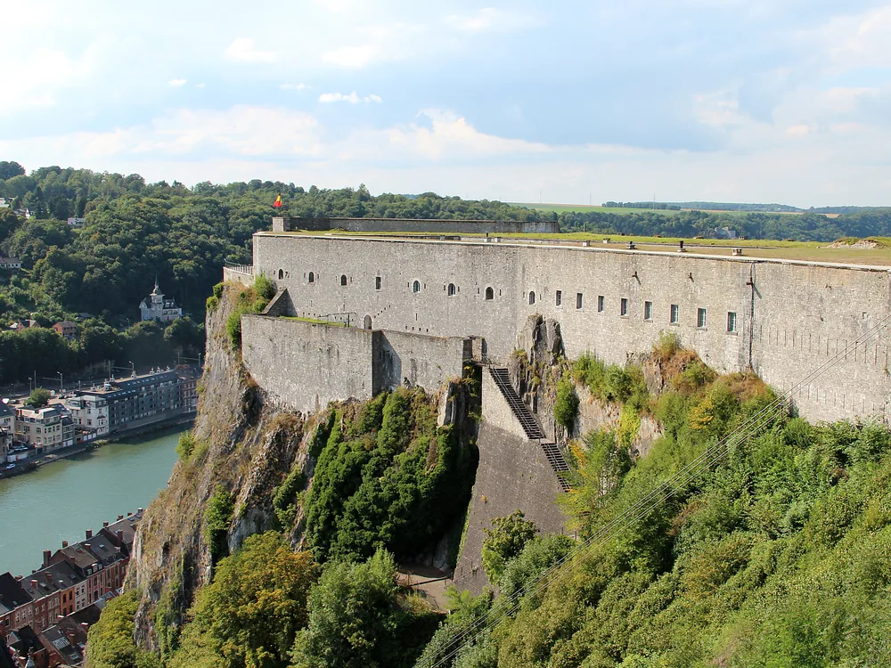 Citadel of Dinant (Citadelle de Dinant) on its 100-metre limestone cliff above the Meuse in Wallonia, Belgium — the star-plan fortress built 1818–21, with the collegiate church of Notre-Dame and cable car at the cliff base