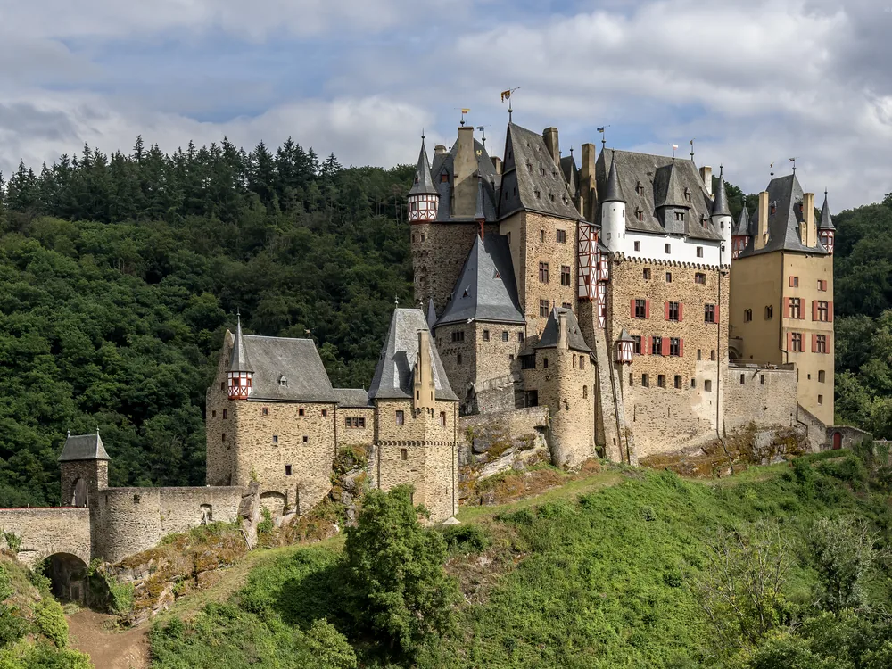 Burg Eltz rising from the forested Moselle Valley hills in morning mist