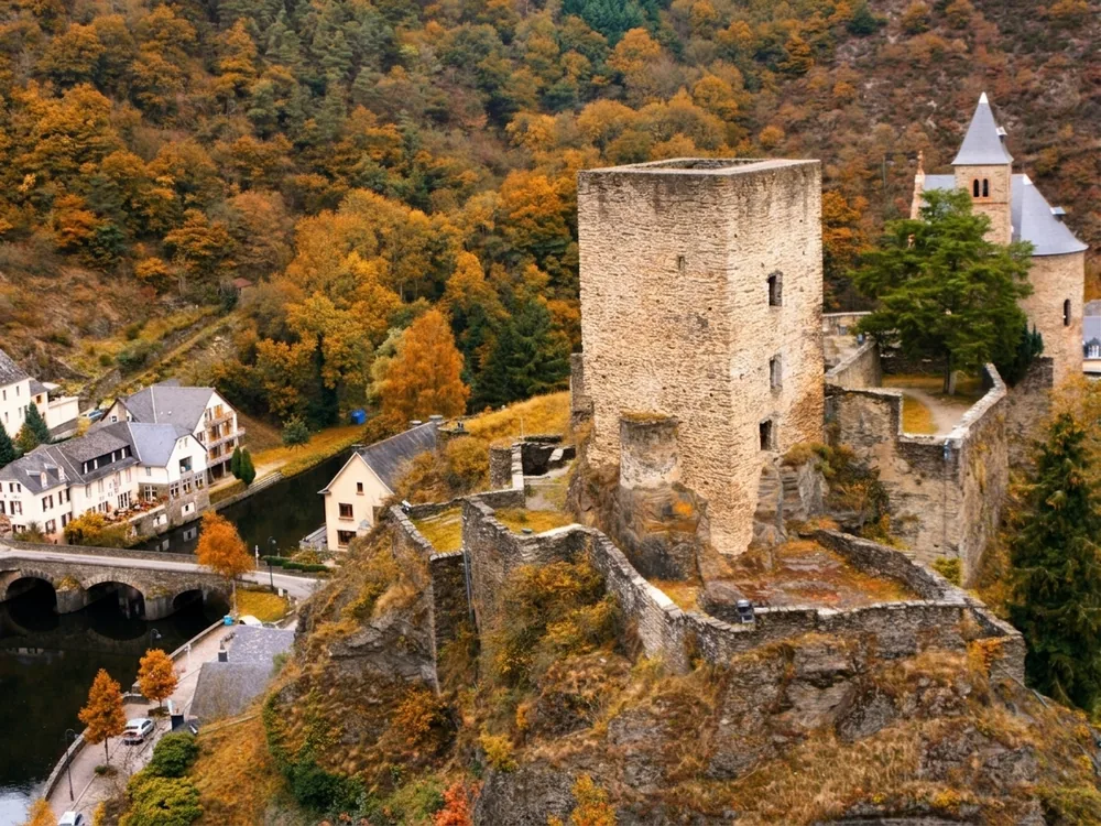 Esch-sur-Sûre Castle ruin on the limestone cliff above the medieval village and the dramatic Sûre river loop in Luxembourg — a 10th-century fortress ruin with free open access