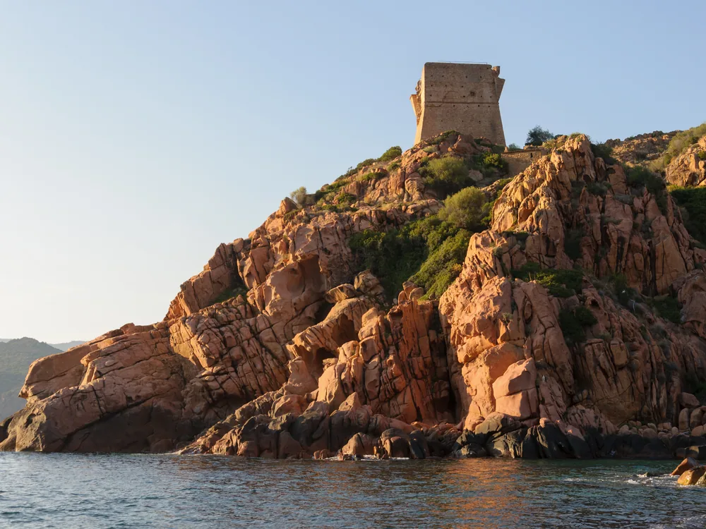 Genoese Tower at Porto, Corsica — the 16th-century cylindrical watchtower on a red granite promontory above the Gulf of Porto, part of the UNESCO World Heritage coastal landscape