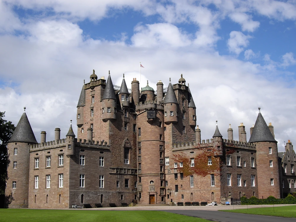 Glamis Castle's Scottish Baronial towers and conical turrets rising above a tree-lined avenue in Angus on a clear summer morning