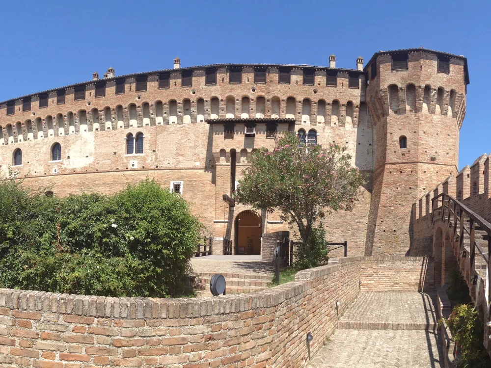 The Rocca di Gradara and its walled medieval borgo on a hilltop in the Marche, with towers and curtain walls rising above the surrounding countryside