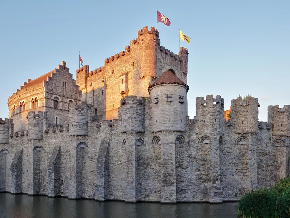 Gravensteen castle rising above the Ghent canals at dusk, with the medieval city roofline behind