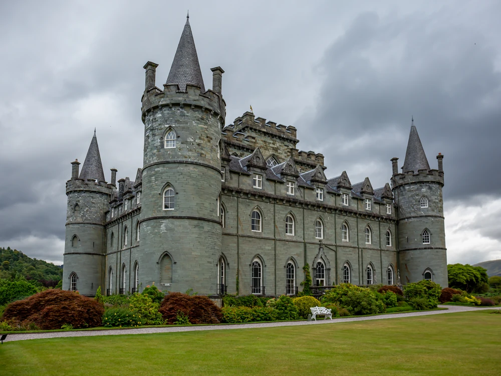 Inveraray Castle's iconic blue-grey turreted facade reflected in the River Aray, surrounded by woodland in Argyll on a still autumn day