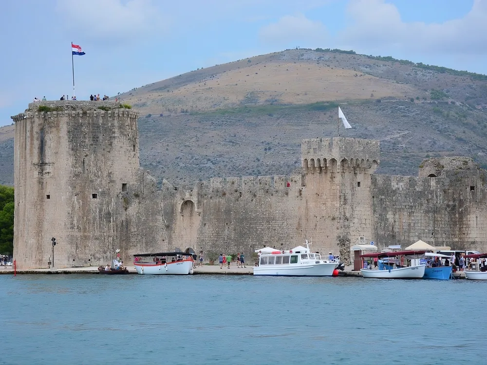 Kamerlengo Castle on the western waterfront of Trogir's UNESCO-listed old town island, Croatia — the 15th-century Venetian fortress with its circular sea tower reflected in the Adriatic channel between Trogir and Čiovo Island