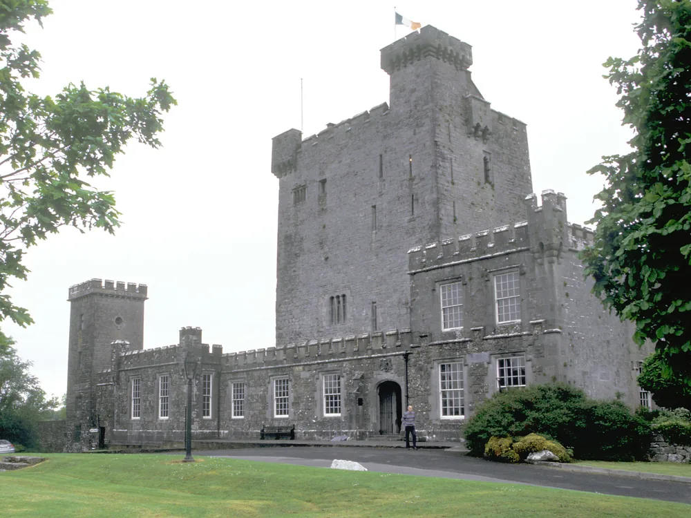 Knappogue Castle's 15th-century tower rising above the County Clare countryside at dusk, lights glowing from the Great Hall windows