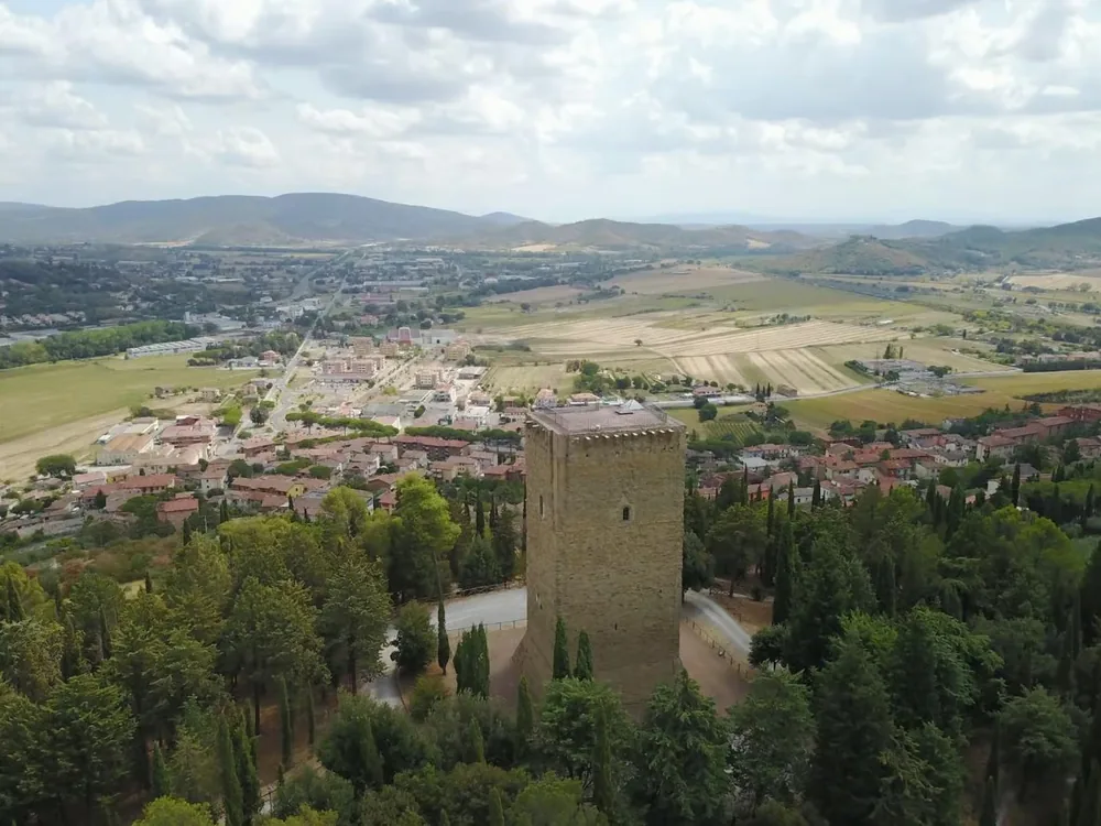 Torre dei Lambardi di Magione — the Knights Hospitaller medieval tower on the forested hillside above Magione, Umbria, with Lake Trasimeno visible in the distance