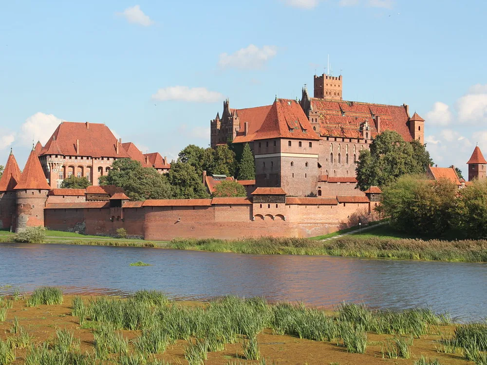 Malbork Castle reflected in the Nogat river at golden hour — the world's largest brick castle in northern Poland