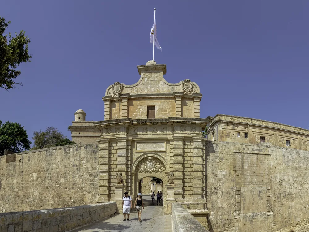 Mdina's Baroque gateway and limestone walls at dusk — the Silent City of Malta perched on its central ridge, with Rabat visible below